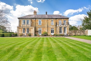 A large stone building with multiple windows, a well-maintained lawn, and a clear sky. - Lodge in Thirsk With Spa & Countryside Views (Thirsk)