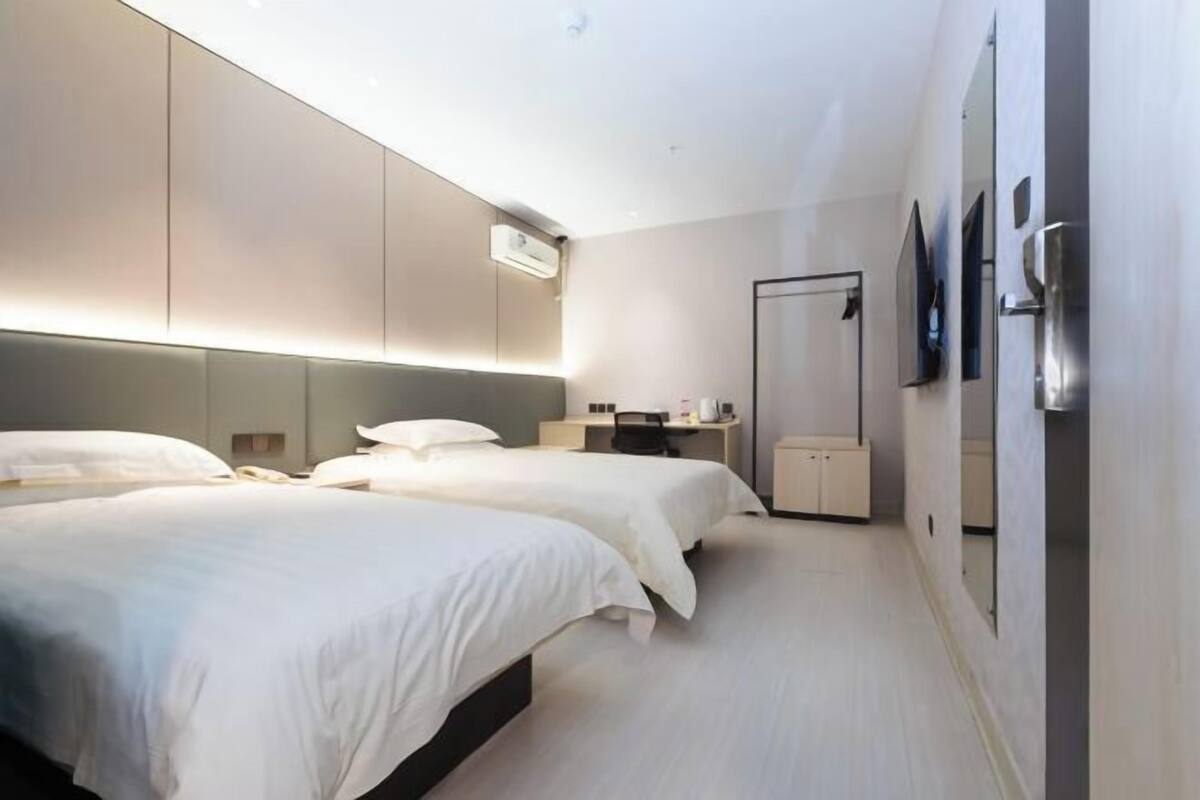 A modern hotel room with two beds, a desk, a chair, a mirror, and a wardrobe.