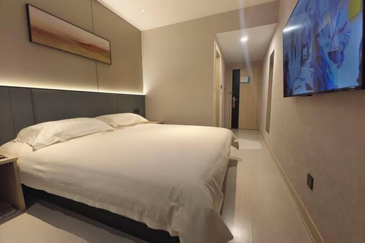 A hotel room with a bed, a nightstand, a painting on the wall, and a TV mounted on the wall.