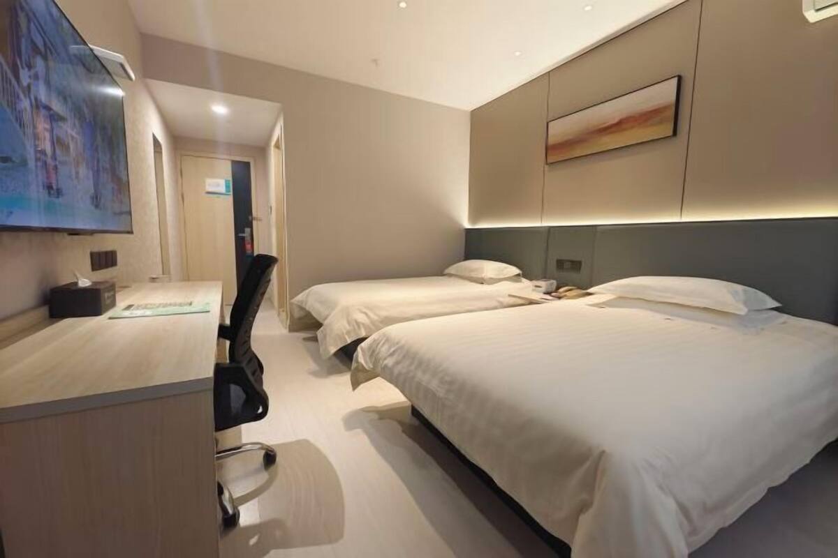A hotel room with two beds, a desk, a chair, a TV, and a painting on the wall.