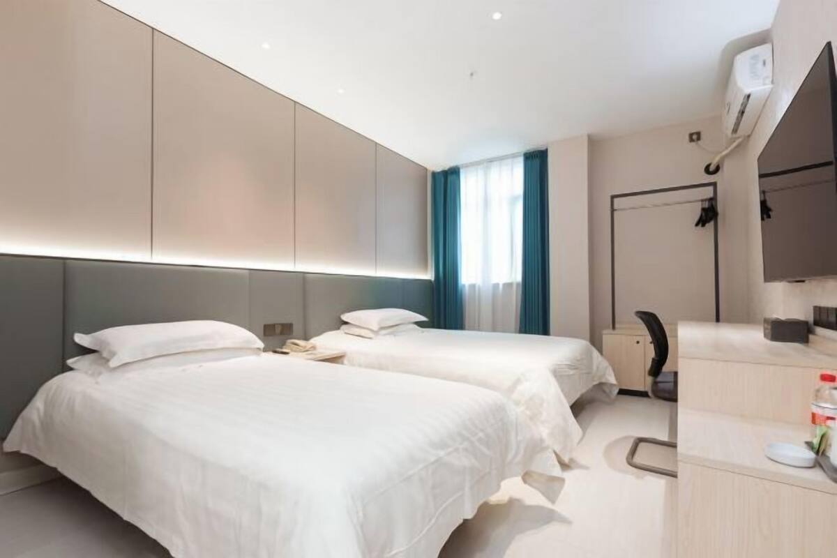 A modern hotel room with two beds, a desk, a chair, and a large mirror.
