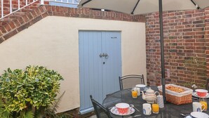 Un patio con una mesa lista para el desayuno, una puerta azul y un muro de ladrillo.