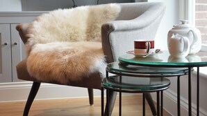Una habitación acogedora con un sillón mullido, una mesita de cristal con tetera y taza, y un televisor montado en la pared.