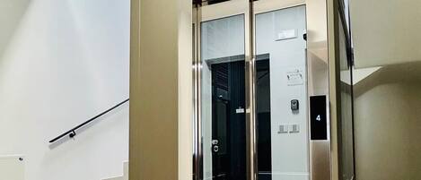 A modern elevator with a glass door, a staircase with a black handrail, and a number 4 sign on the wall.