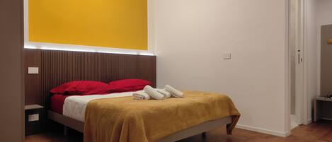 A bedroom with a bed, a nightstand, a wall-mounted light, and a door.