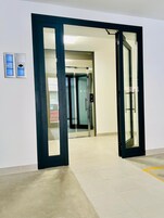 An open door leading to a hallway with a glass elevator and a control panel on the wall.