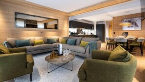 Una sala moderna con un sofá modular, dos sillones, una mesa de centro y un comedor con una mesa preparada para cuatro personas.