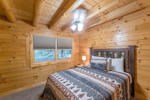 A wooden cabin bedroom with a bed, a window, and a ceiling fan.