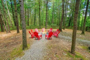 A circular seating area with red chairs around a central fire pit in a forest setting. - Hocking Creek Reserve | Fenced Yard, Pet Friendly (Logan)