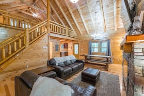 A wooden cabin interior with a staircase, leather sofa, and a stone fireplace.