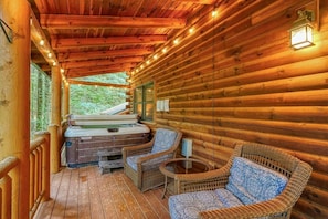 A wooden cabin with a hot tub, wicker chairs, and a wooden deck.
