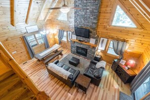 A cozy cabin interior with a stone fireplace, wooden furniture, and large windows. - Hocking Creek Reserve | Fenced Yard, Pet Friendly (Logan)