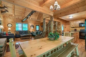 A rustic cabin interior with a wooden dining table, sofas, a staircase, and a kitchen area. - Buckeye Trail | Hocking Hills, 5BR, Hot Tub, Pets (Rockbridge)