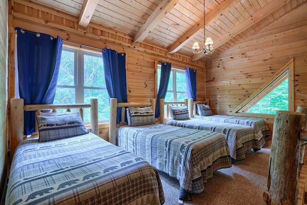 A cabin with three wooden beds, blue curtains, and a sloped ceiling. - Buckeye Trail | Hocking Hills, 5BR, Hot Tub, Pets (Rockbridge)
