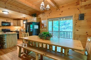 A wooden cabin with a kitchen featuring a refrigerator, microwave, and wooden cabinets. There is a dining table with benches and a window overlooking a forested area. - Buckeye Trail | Hocking Hills, 5BR, Hot Tub, Pets (Rockbridge)