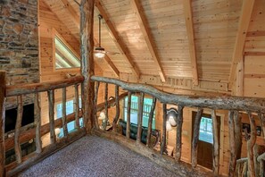 A wooden interior with a stone wall, wooden beams, and a log railing.
