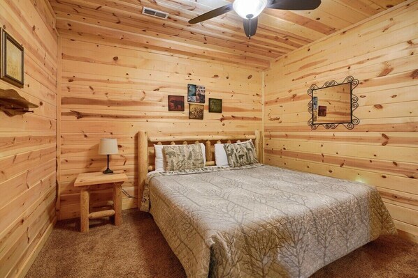 A cozy wooden cabin bedroom with a bed, a nightstand, a lamp, and a ceiling fan.