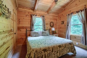 A wooden cabin bedroom with a bed, curtains, a nightstand, and a window. - Buckeye Trail | Hocking Hills, 5BR, Hot Tub, Pets (Rockbridge)