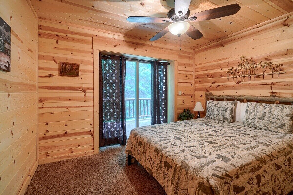 A wooden cabin bedroom with a bed, a ceiling fan, and a window with curtains.