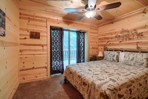 A wooden cabin bedroom with a bed, a ceiling fan, and a window with curtains. - Buckeye Trail | Hocking Hills, 5BR, Hot Tub, Pets (Rockbridge)
