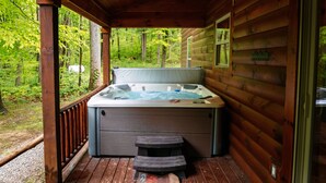 A wooden cabin with a hot tub on a deck, surrounded by a forest. - Bear Crossing | Hocking Hills, Sleeps 10, Pets (Logan)