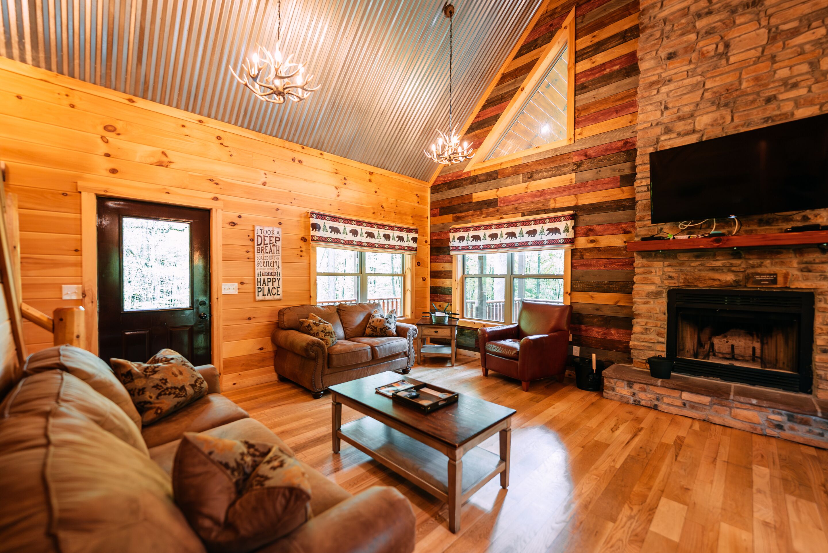 L’intérieur d’une cabane en rondins, avec un plafond en bois, une cheminée, un téléviseur fixé au mur et un coin salon confortable comprenant un canapé et une table basse.