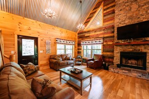 A log cabin interior with a wooden ceiling, a fireplace, a TV mounted on the wall, and a cozy seating area with a sofa and a coffee table. - Bear Crossing | Hocking Hills, Sleeps 10, Pets (Logan)