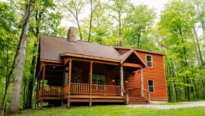 A wooden cabin with a porch, surrounded by trees.