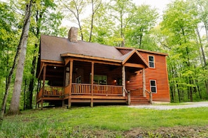 A wooden cabin with a porch, surrounded by trees.