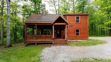 Une cabane en rondins avec un porche, une cheminée et une allée gravillonnée.