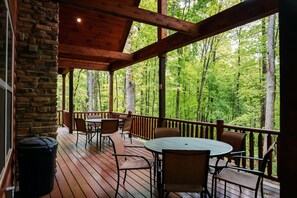 A covered outdoor deck with wooden furniture and a stone wall.