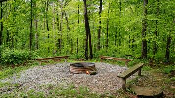 Un terrain de camping boisé, doté d’un foyer circulaire, de deux bancs et d’un sol rocheux.