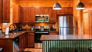 A wooden cabin-style kitchen with wooden cabinets, stainless steel appliances, and a granite countertop.