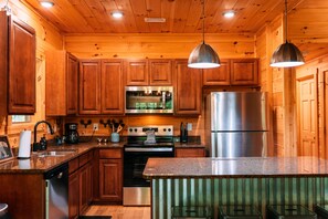 A wooden cabin-style kitchen with wooden cabinets, stainless steel appliances, and a granite countertop.
