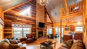 A log cabin interior with a fireplace, wooden furniture, and a loft dining area. - Bear Crossing | Hocking Hills, Sleeps 10, Pets (Logan)