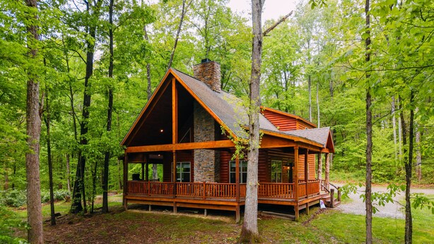 A cabin with a stone chimney, wooden deck, and surrounded by trees. - Bear Crossing | Hocking Hills, Sleeps 10, Pets (Logan)