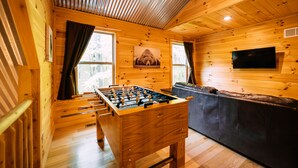 A wooden interior with a foosball table, a sofa, and a television. - Bear Crossing | Hocking Hills, Sleeps 10, Pets (Logan)