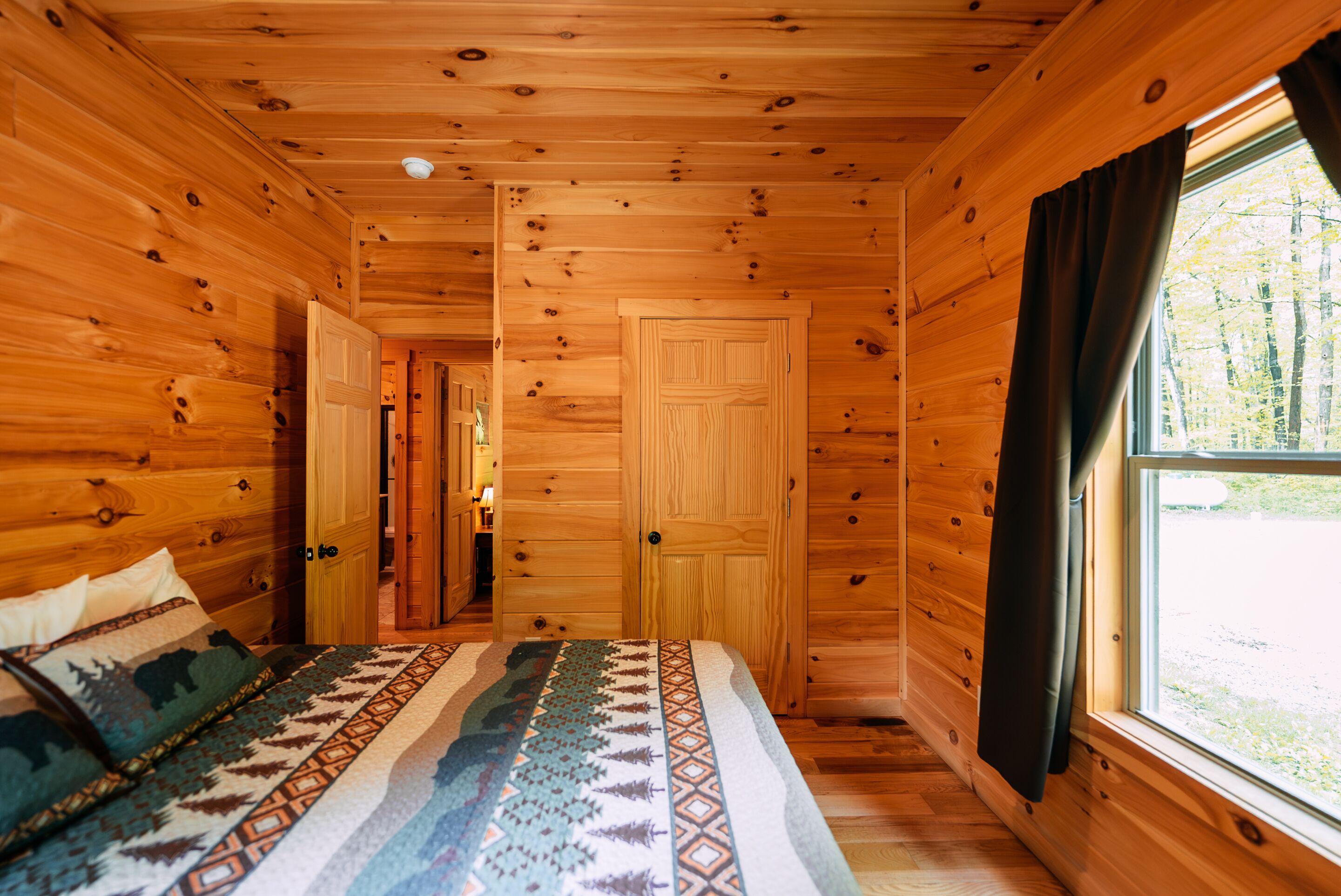 L’intérieur d’une cabane en bois, avec un lit, une fenêtre et une porte.