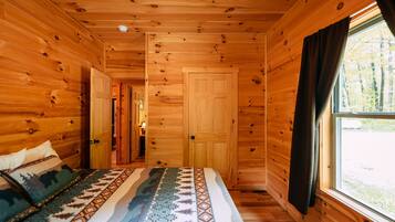 L’intérieur d’une cabane en bois, avec un lit, une fenêtre et une porte.