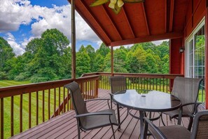 A wooden deck with a glass table and chairs, overlooking a lush green landscape.