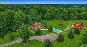 Experience a serene farmhouse retreat surrounded by lush greenery and a well-maintained lawn, featuring a swimming pool and a gabled roof.