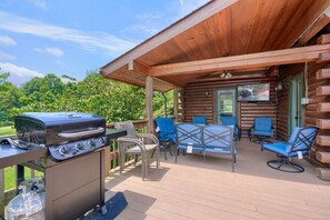 Eine überdachte Terrasse im Freien mit Grill, Stühlen und einem Fernseher.