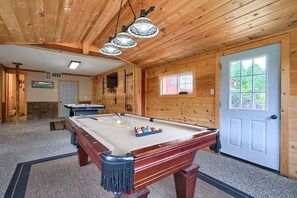 A pool table in a wooden room with a door, a window, and a fireplace.