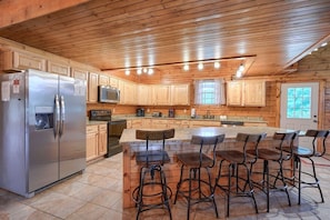 A spacious kitchen with wooden cabinets, a stainless steel refrigerator, a microwave, and a central island with bar stools.