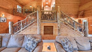 Ein Blockhaushaus-Interieur mit einer zentralen Treppe, einer Couch mit gemusterten Kissen und einem kleinen Tisch mit Fernbedienung.