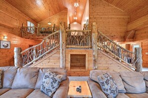A log cabin interior with a central staircase, a sofa with patterned cushions, and a small table with a remote control.