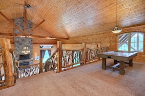 A cozy lodge interior with a stone fireplace, a pool table, and a rustic wooden ceiling.
