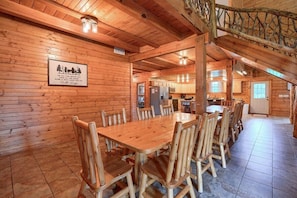A wooden interior with a large dining table and chairs, a kitchen area, and a staircase.