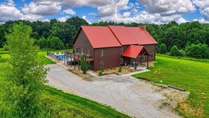 A large wooden house with a red roof, a swimming pool, and a well-maintained lawn.