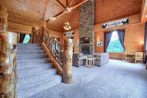 A log cabin interior with a stone fireplace, a staircase, a sofa, and a dining table.